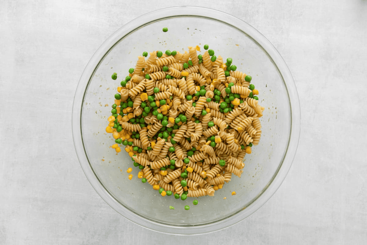 Combining peas and corn with pasta in a glass bowl.
