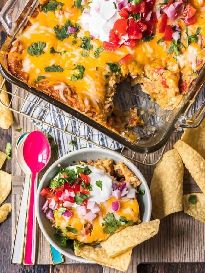 overhead view of king ranch chicken casserole, next to a bowl filled with a serving of the casserole and topped with red onions, tomatoes, and sour cream