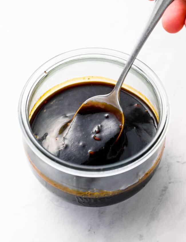 three-quarters view of a spoon stirring korean bbq sauce in a glass bowl.