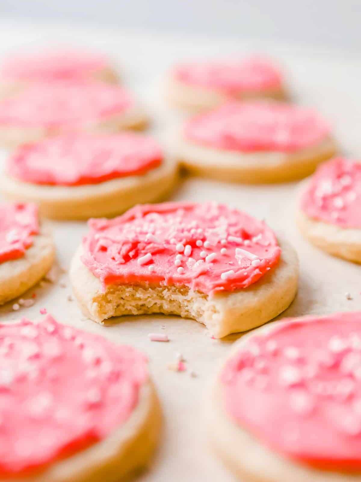 close up of a bitten pink frosted lofthouse cookie surrounded by more cookies.