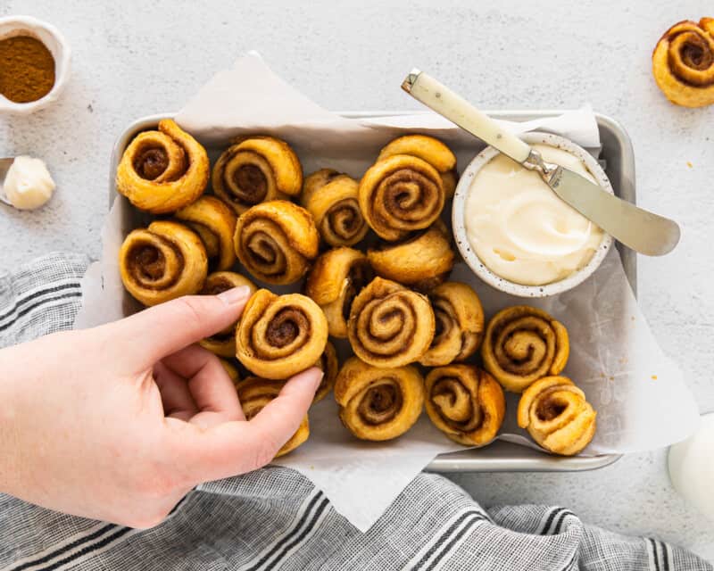 overhead view of a hand grabbing a mini cinnamon roll from a serving tray.