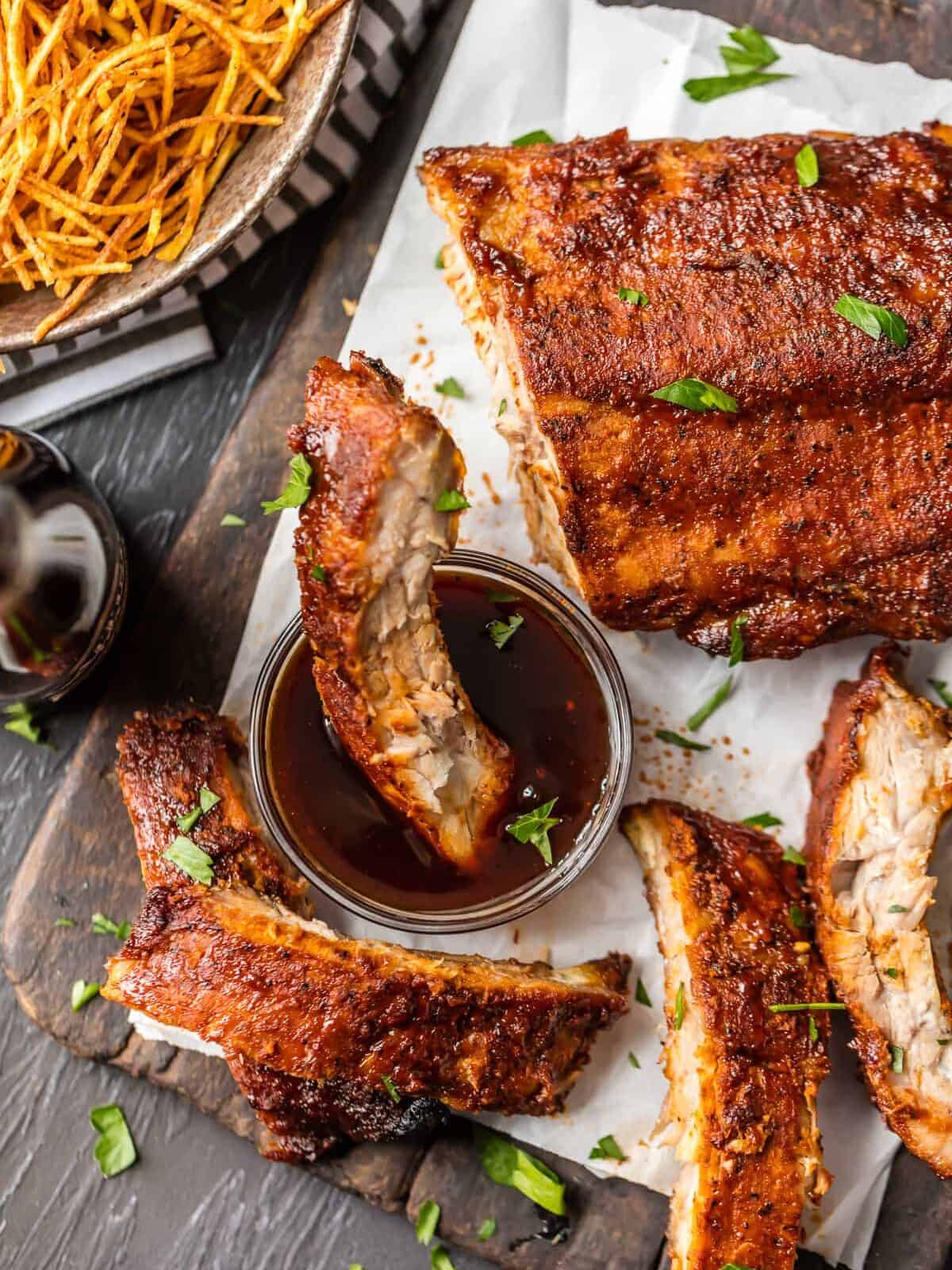 OVEN BAKED RIBS are just sooo tasty. I like cooking ribs in the oven because it's super easy and they turn out so moist. They're also great for rainy days when you don't have access to your grill. These dry rubbed ribs are one of our favorite easy dinners for summer. So kick your BBQ skills up a notch with these Easy Oven Baked Ribs, whether you're making spare ribs or baby back ribs! Either way, you're left with SO MUCH FLAVOR! Easy Oven baked ribs, one rib dipped in bbq sauce