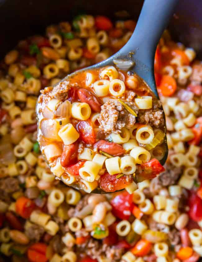close up view of a spoonful of pasta e fagioli soup above a pot.