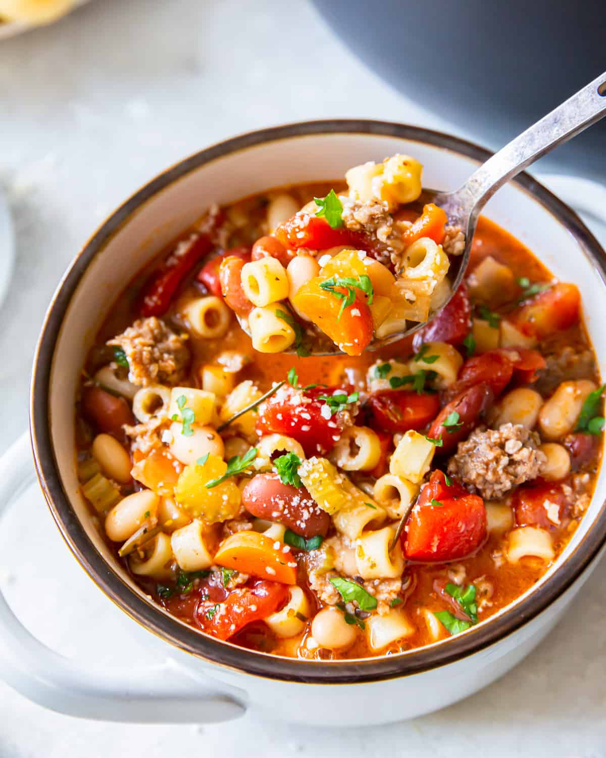 three-quarters view of a serving of pasta e fagioli soup in a white tureen with a spoon.