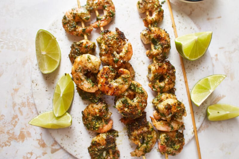 close-up overhead view of 4 pesto shrimp skewers on a white plate.