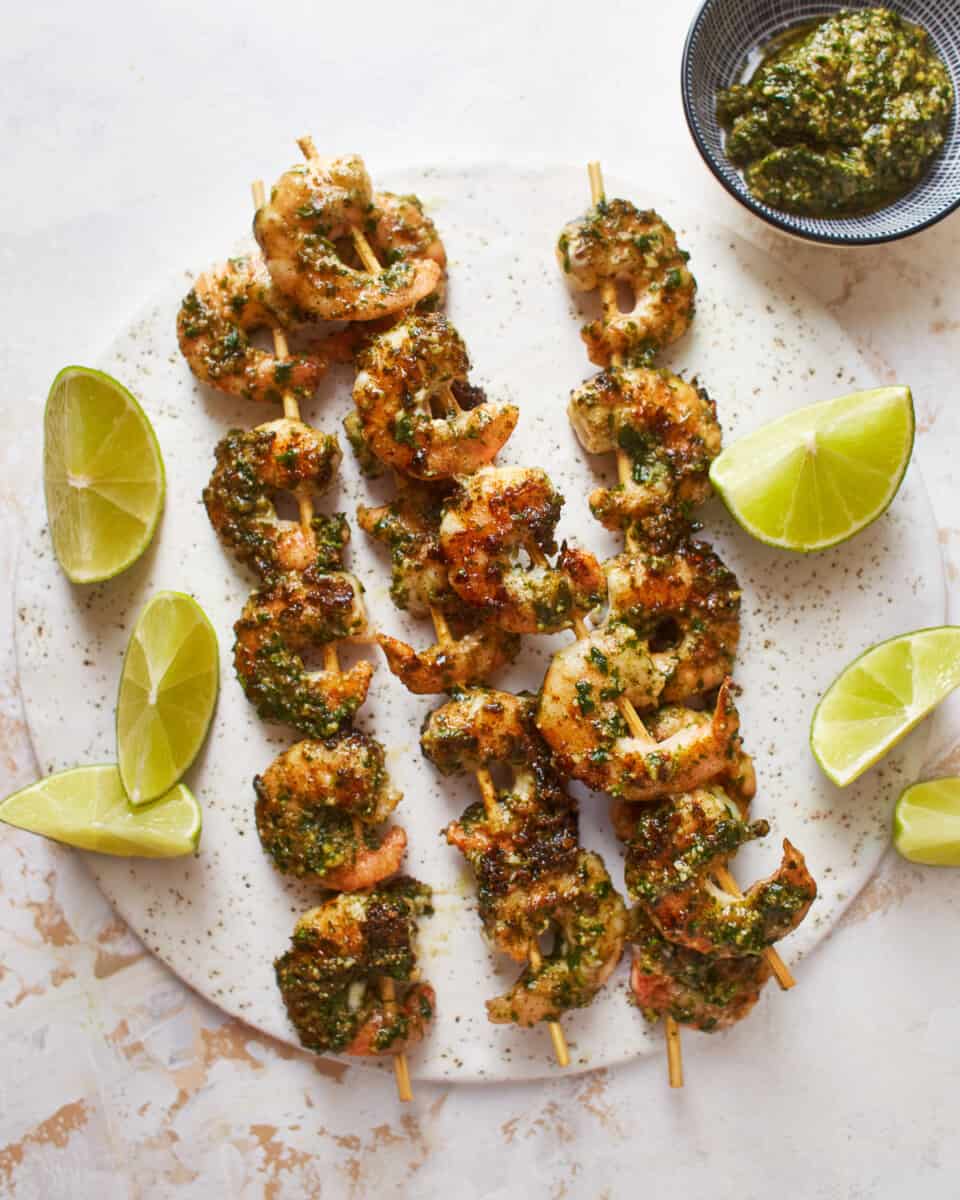 overhead view of 4 pesto shrimp skewers on a white plate.
