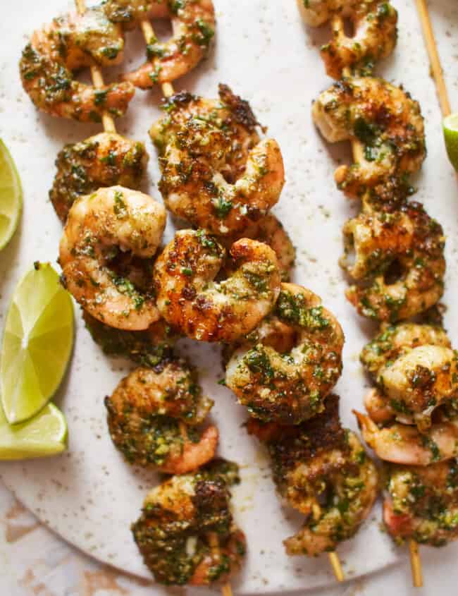 close-up view of 4 pesto shrimp skewers on a white plate.