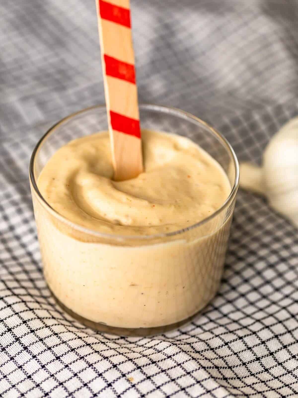 small glass bowl full of creamy aioli, with a red-striped wooden stick