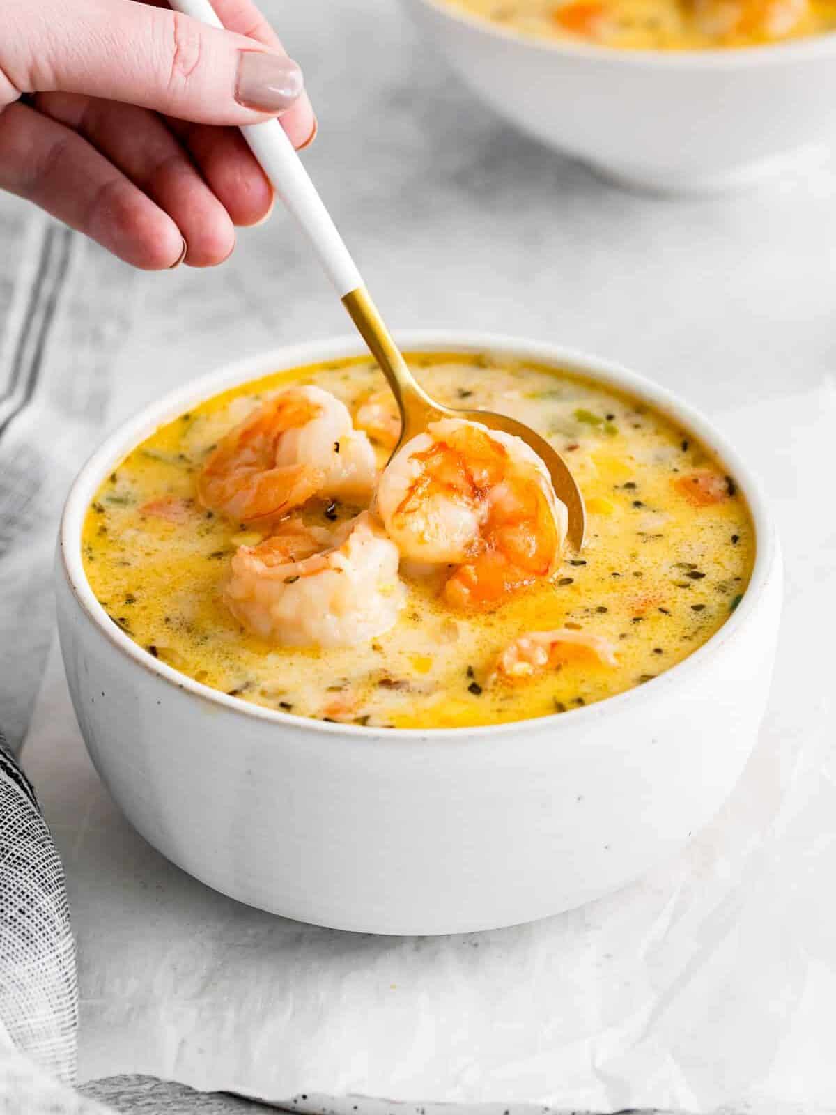 a spoon scooping a shrimp from shrimp corn chowder in a white bowl.