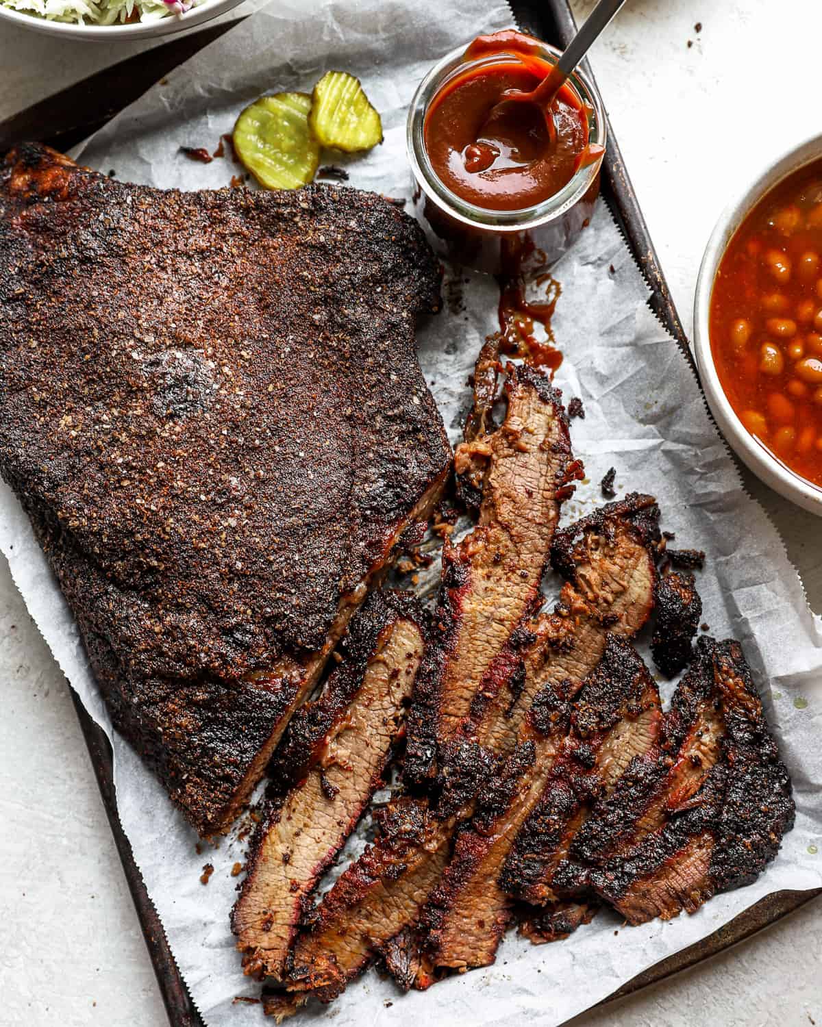 a smoked brisket partially cut into thin slices, on a parchment-lined tray.