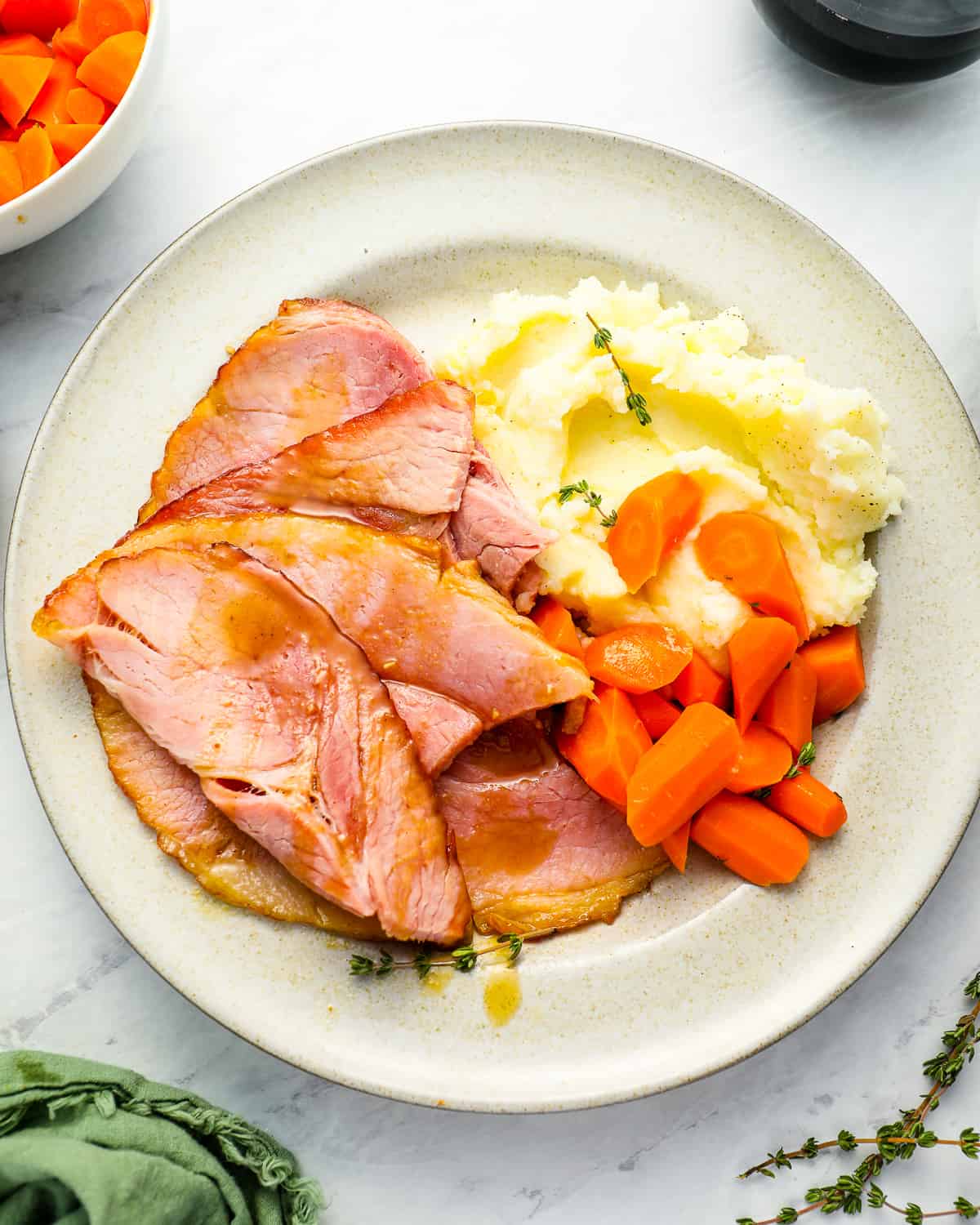 overhead view of a serving of slices of smoked ham on a white plate with mashed potatoes and carrots.
