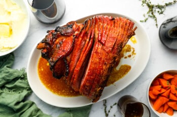 overhead view of a smoked ham on a white oval platter.