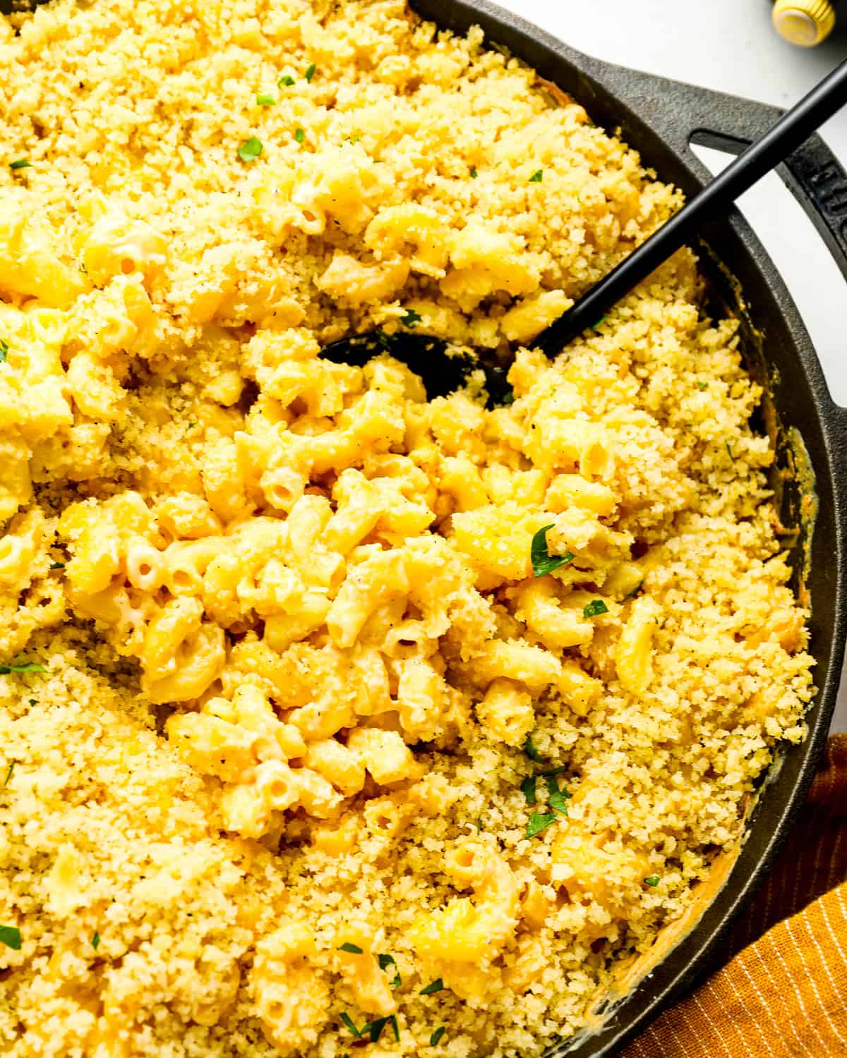 close up overhead view of smoked mac and cheese with gouda and breadcrumbs, in a cast iron skillet with a serving spoon.