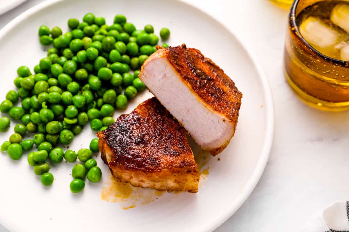 three-quarters view of a halved smoked pork chop on a white plate with peas.
