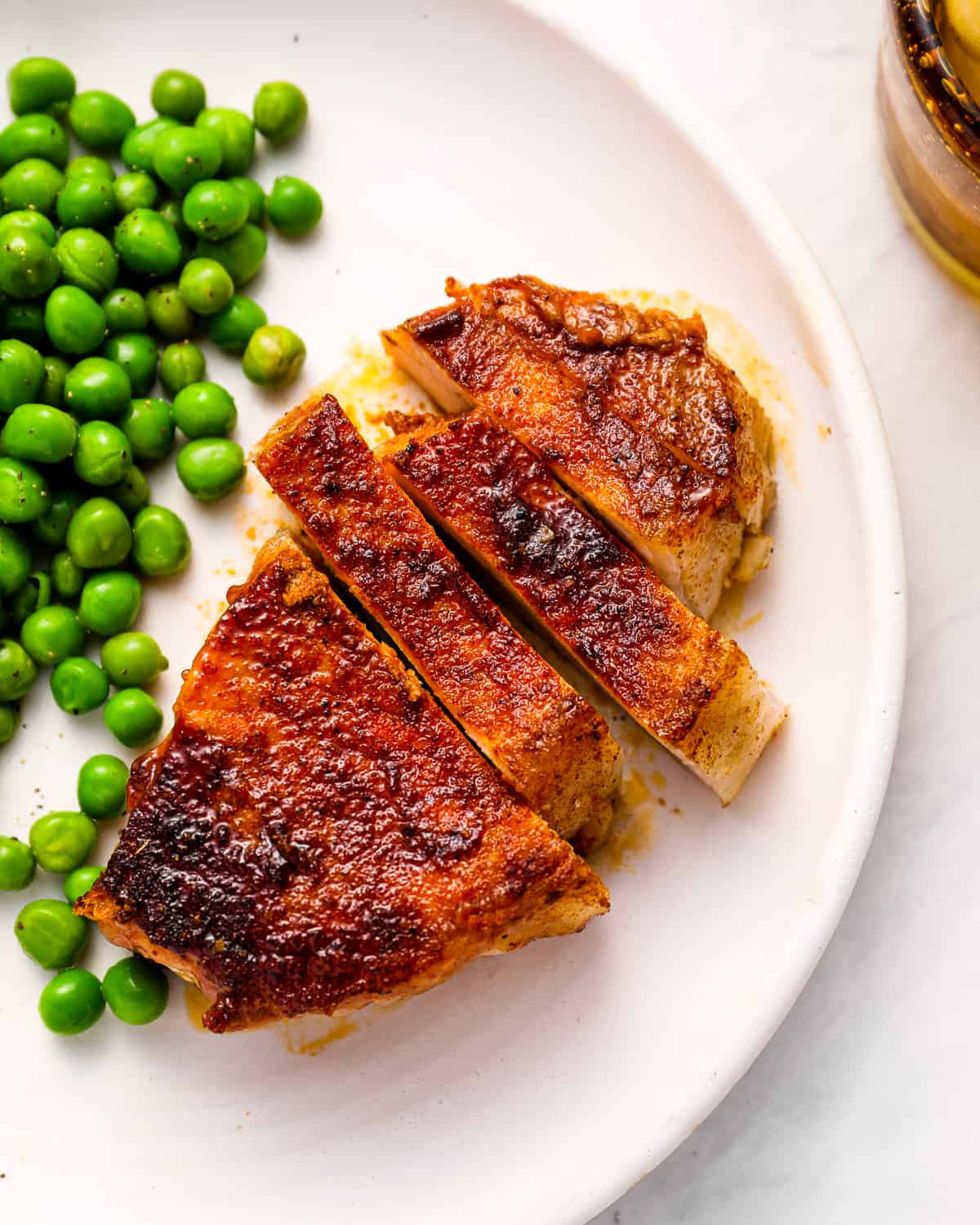 overhead view of a sliced smoked pork chop on a white plate with peas.