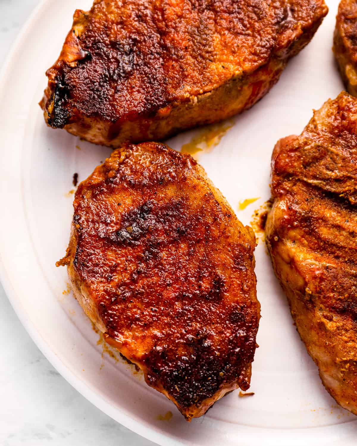 close-up overhead view of smoked pork chops on a white plate.