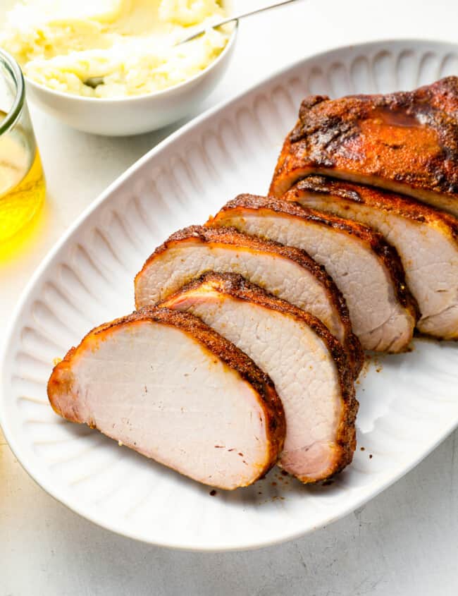 three-quarters view of a sliced smoked pork loin on a white oval serving platter.