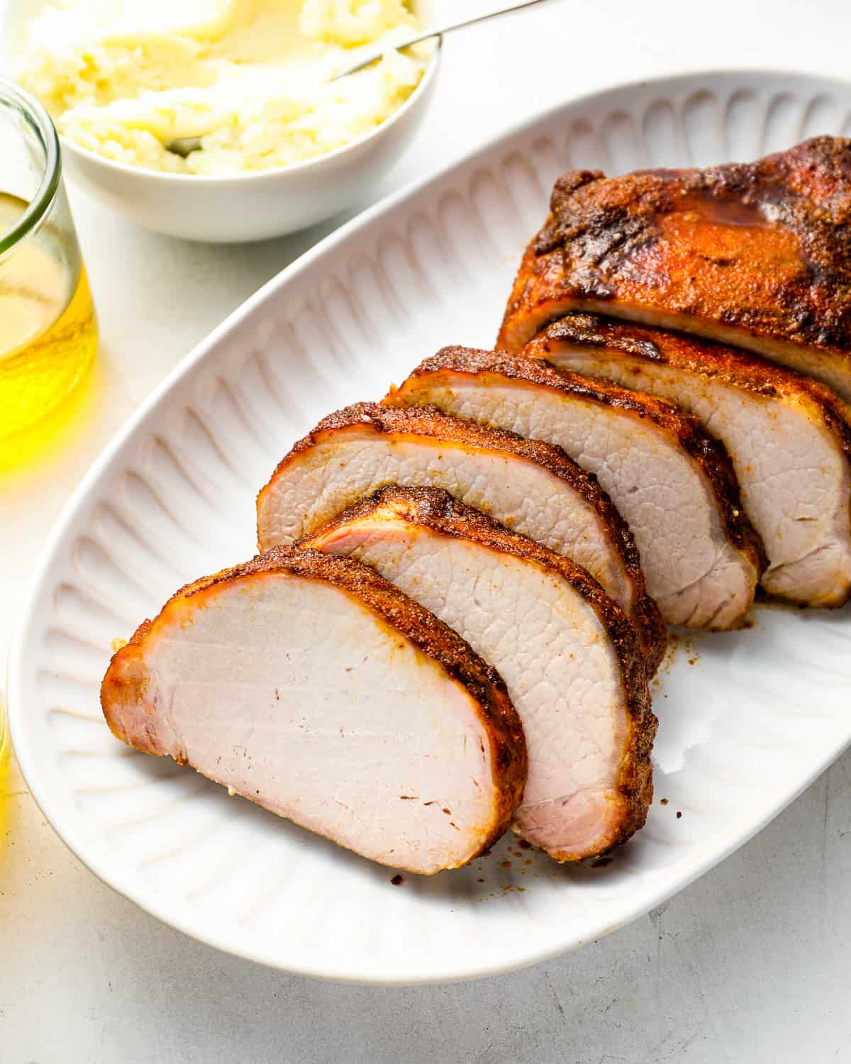 three-quarters view of a sliced smoked pork loin on a white oval serving platter.