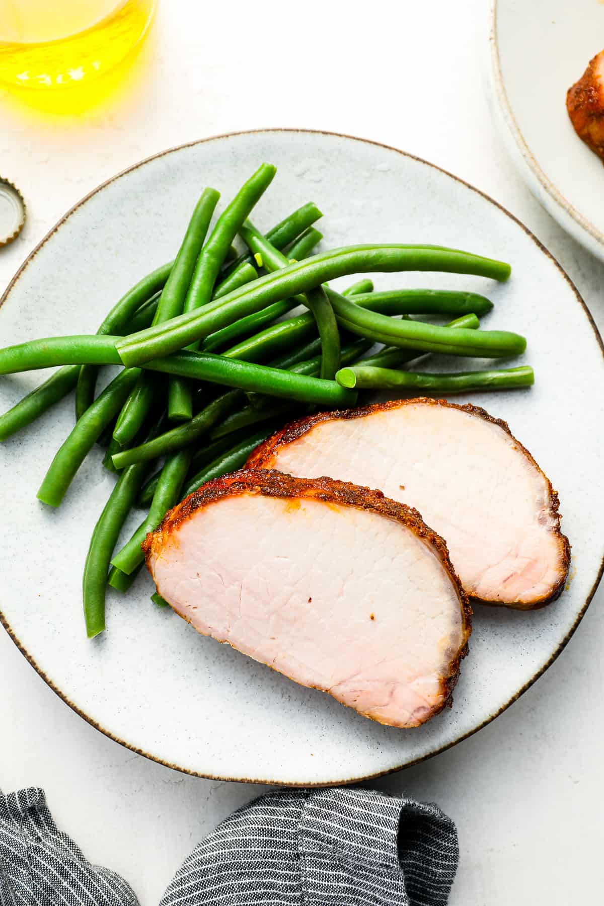 overhead view of 2 slices of smoked pork loin on a white plate with green beans.