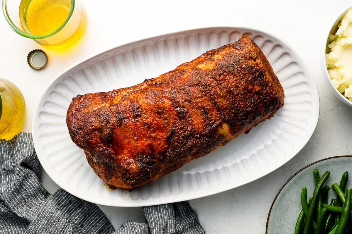 overhead view of a seasoned, smoked pork loin on a white oval serving platter.