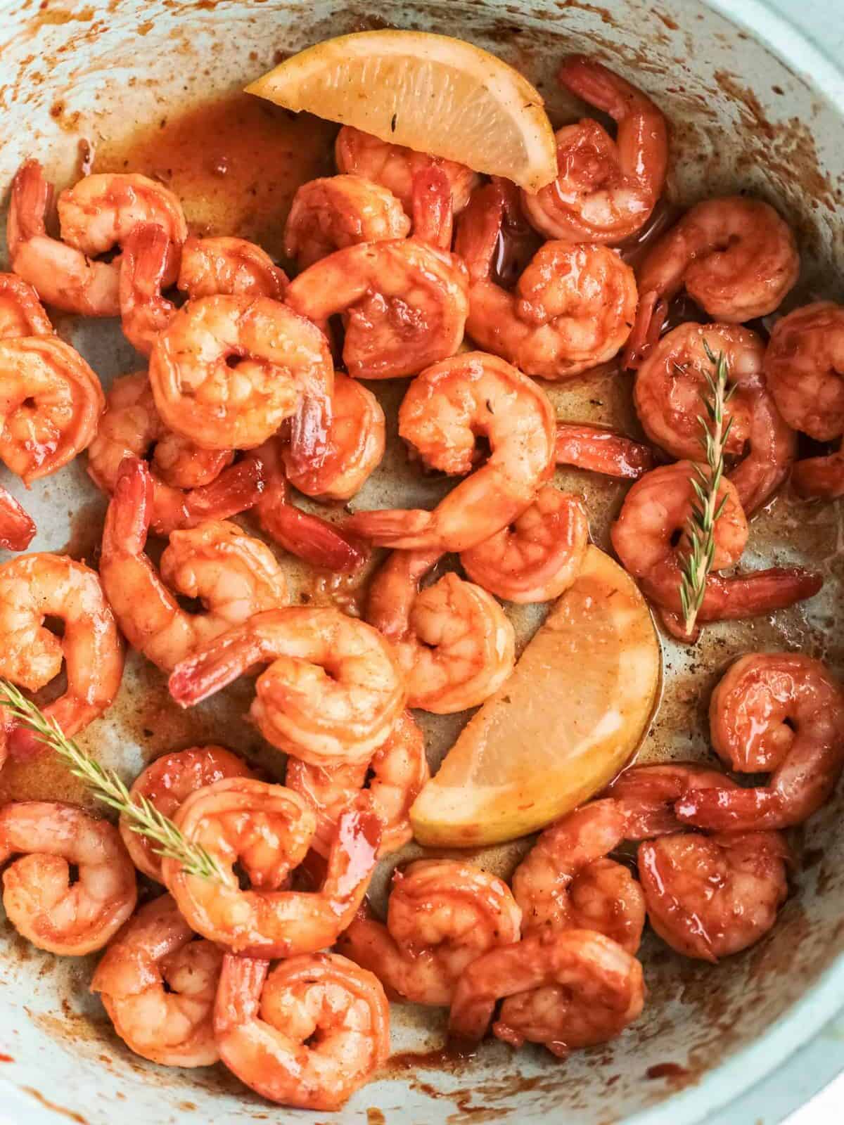 close up of spicy mexican shrimp in a blue bowl with lemon wedges.