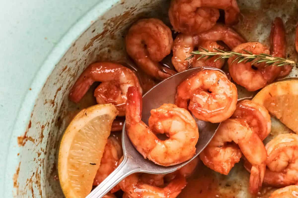 close up of a spoon scooping 2 spicy mexican shrimp from a blue bowl.