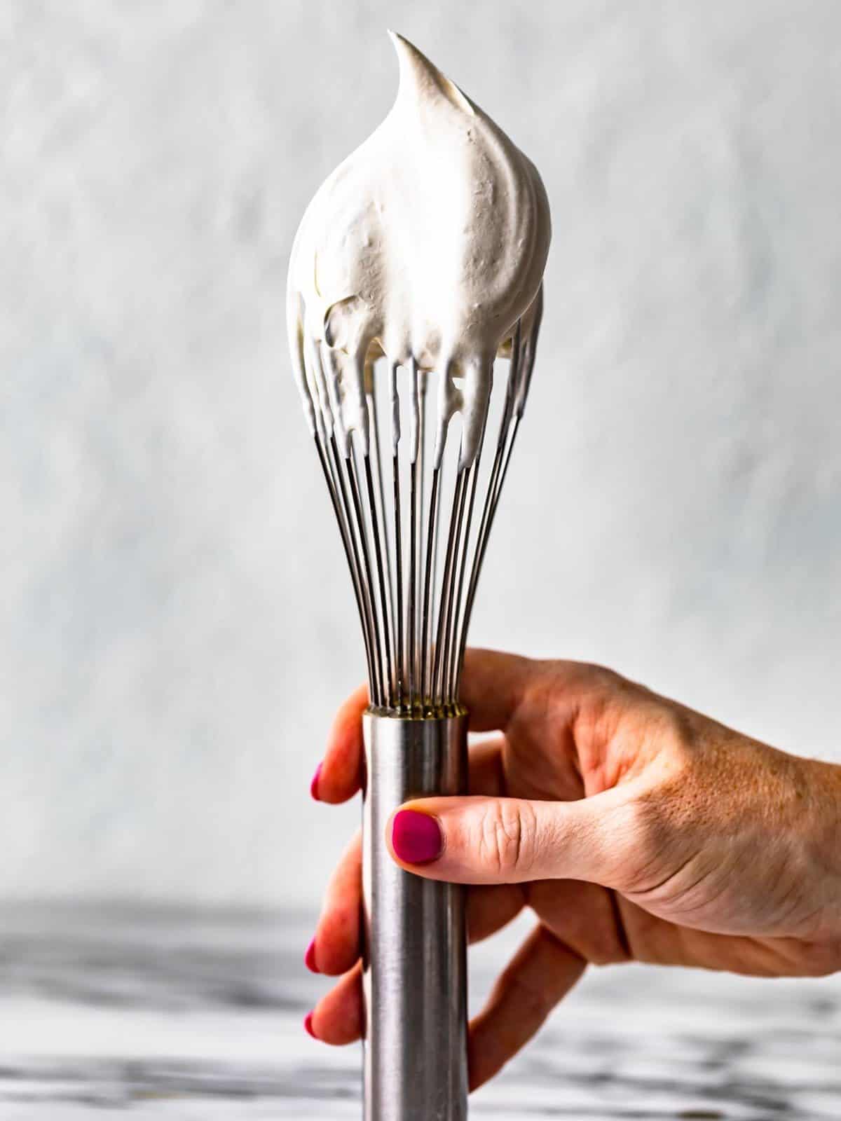 hand holding a whisk dipped in whipped cream