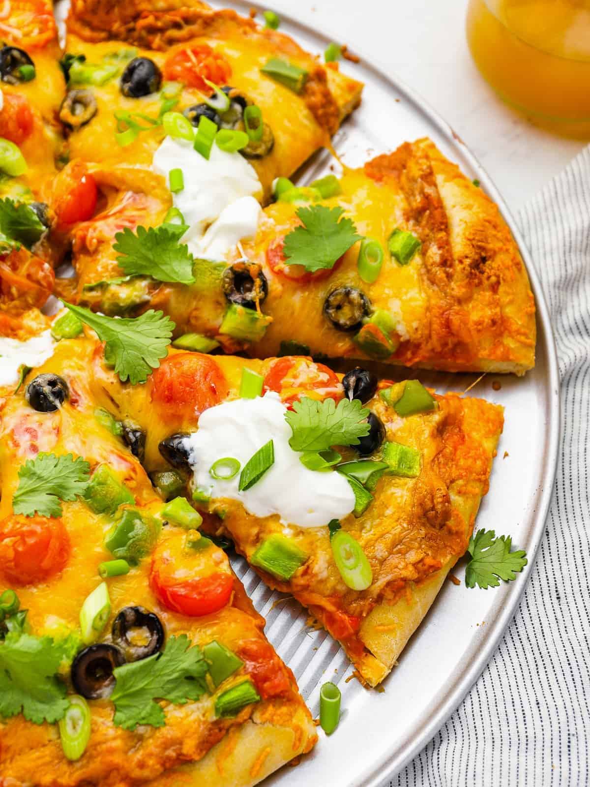 partial view of a sliced taco pizza on a pizza pan.