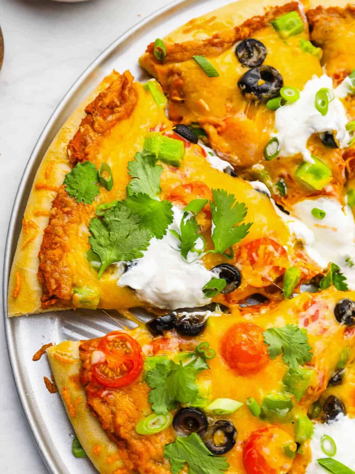 partial view of a sliced taco pizza on a pizza pan.