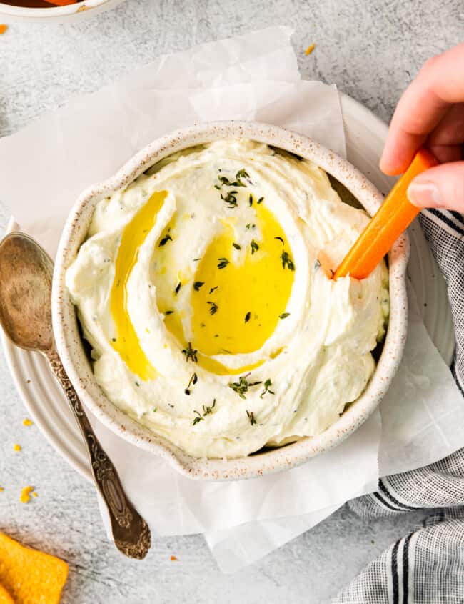 overhead view of a hand dipping a carrot stick into whipped feta dip with olive oil on top.