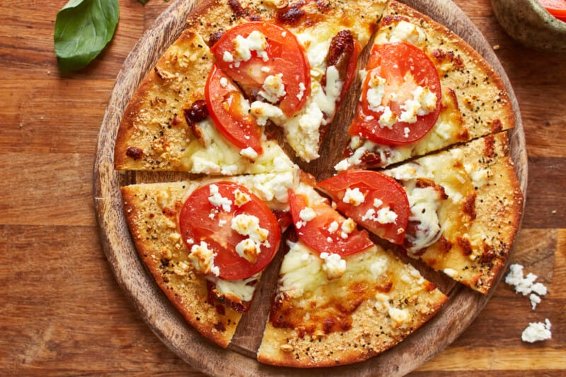 overhead view of a cut white pizza on a round wooden cutting board.