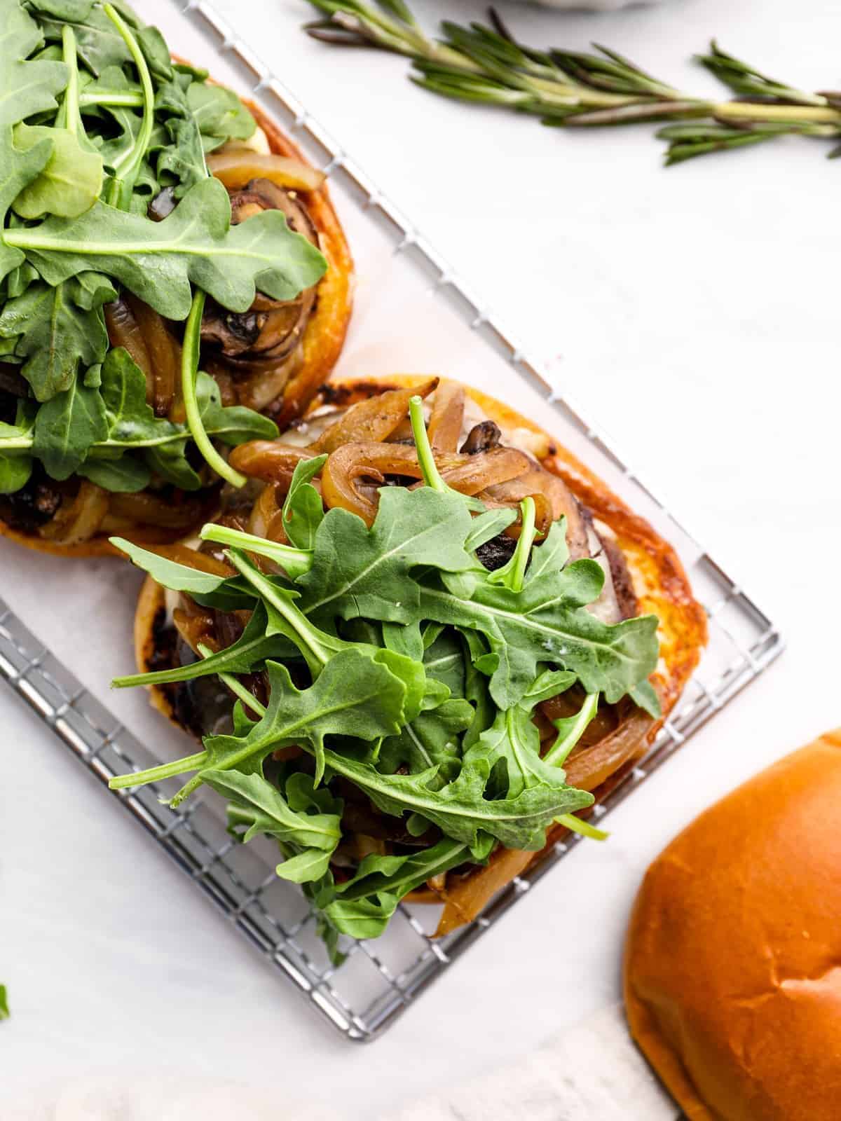 overhead view of hamburgers being assembled, piled up with mushrooms, Swiss cheese, and arugula