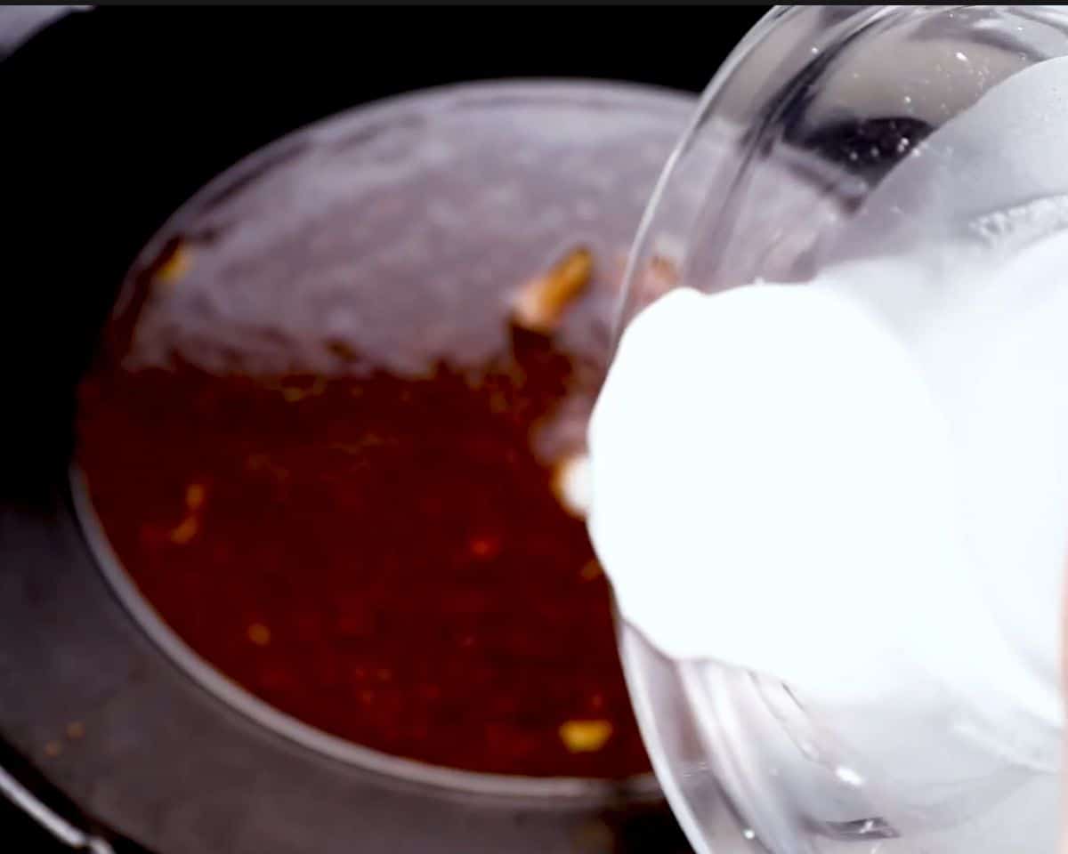 Pouring a cornstarch slurry into a glossy honey garlic sauce to thicken it in a saucepan