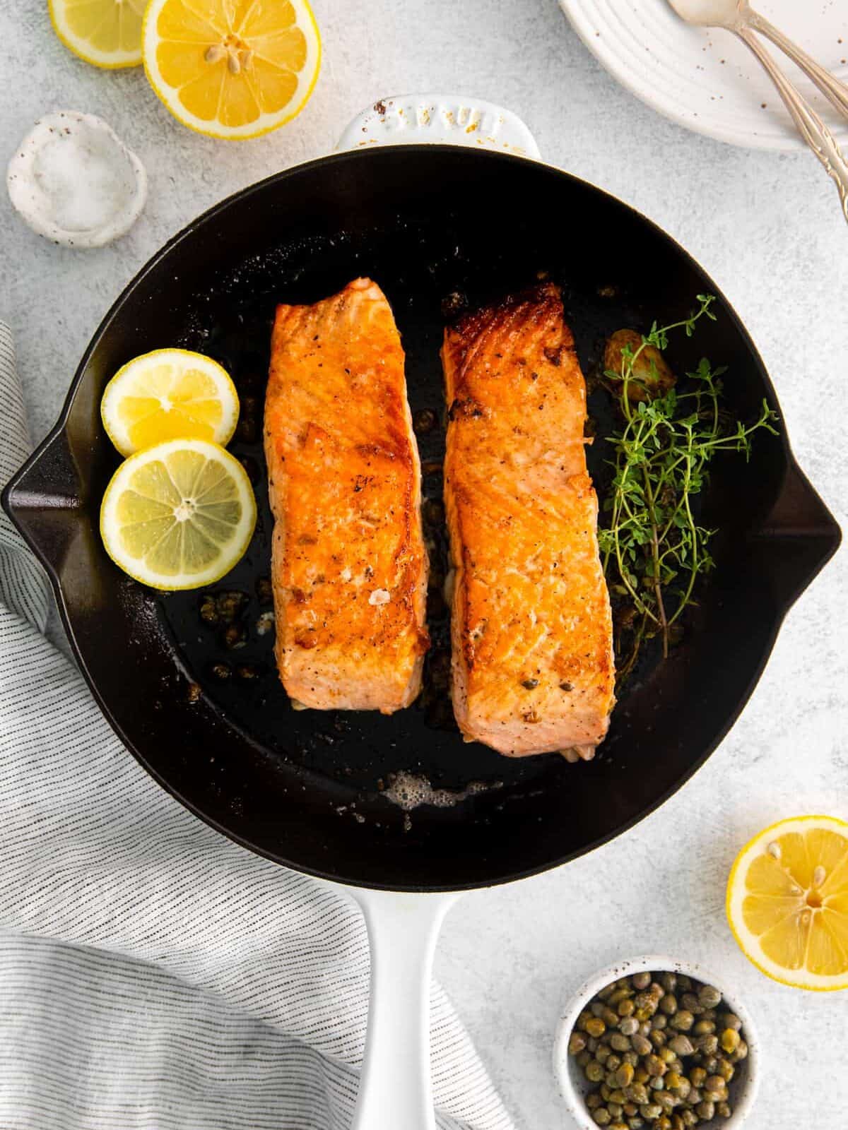 2 cooked salmon filets in a cast iron skillet with thyme and lemon.