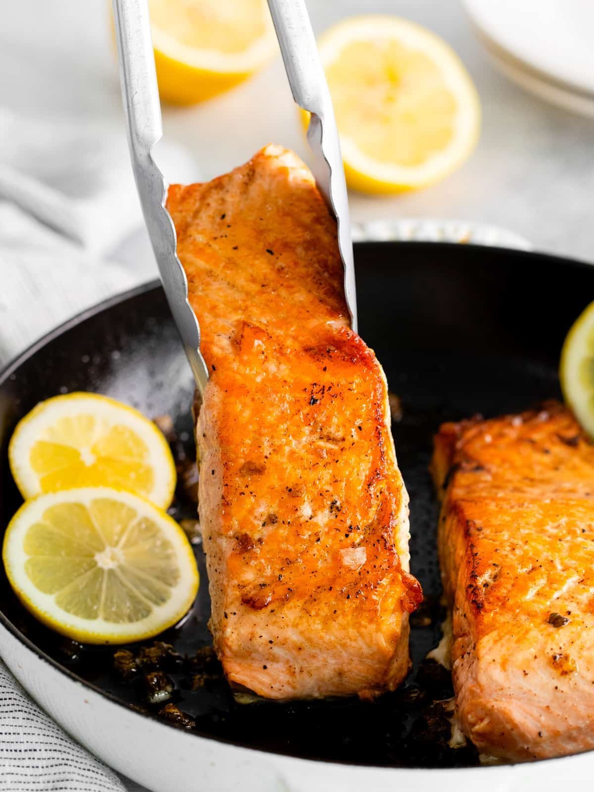 tongs grabbing a salmon filet from a cast iron pan.