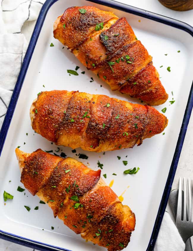 three chicken breasts on a baking tray with a fork.