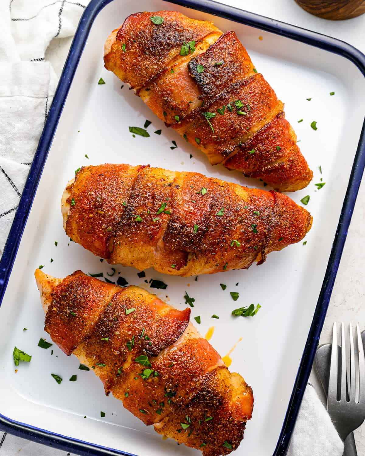 three bacon wrapped chicken breasts on a baking tray with a fork.