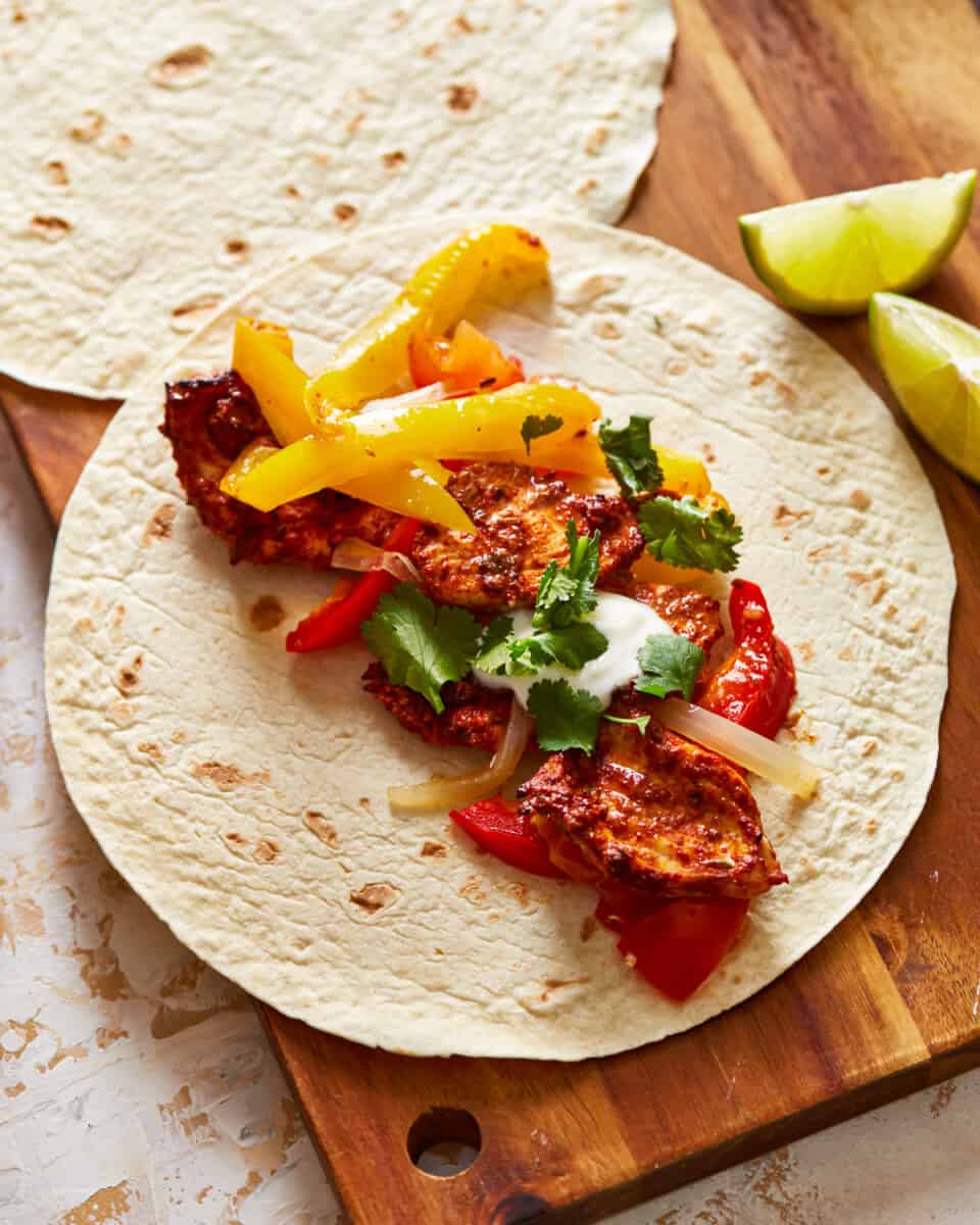 a tortilla with chicken and peppers on a wooden cutting board.