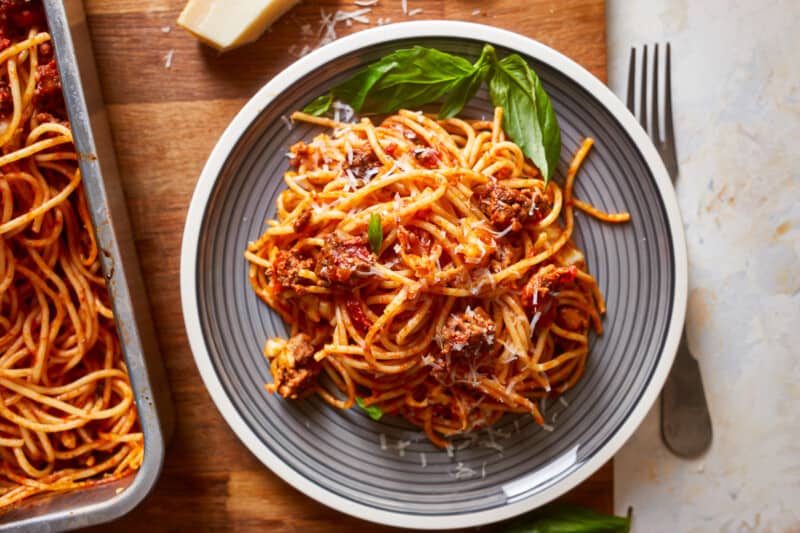 a plate of spaghetti and meatballs on a wooden cutting board.