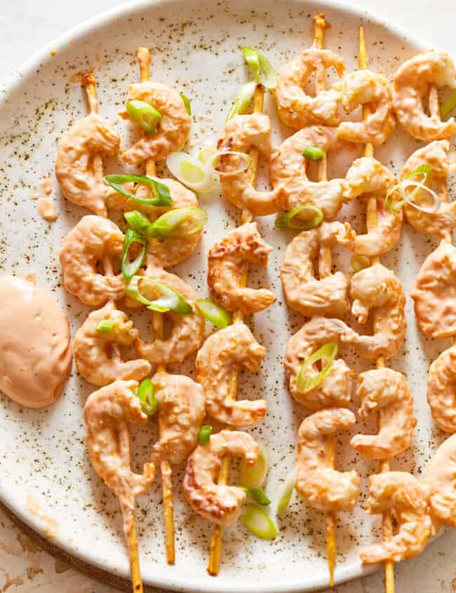 shrimp skewers with dipping sauce on a plate.