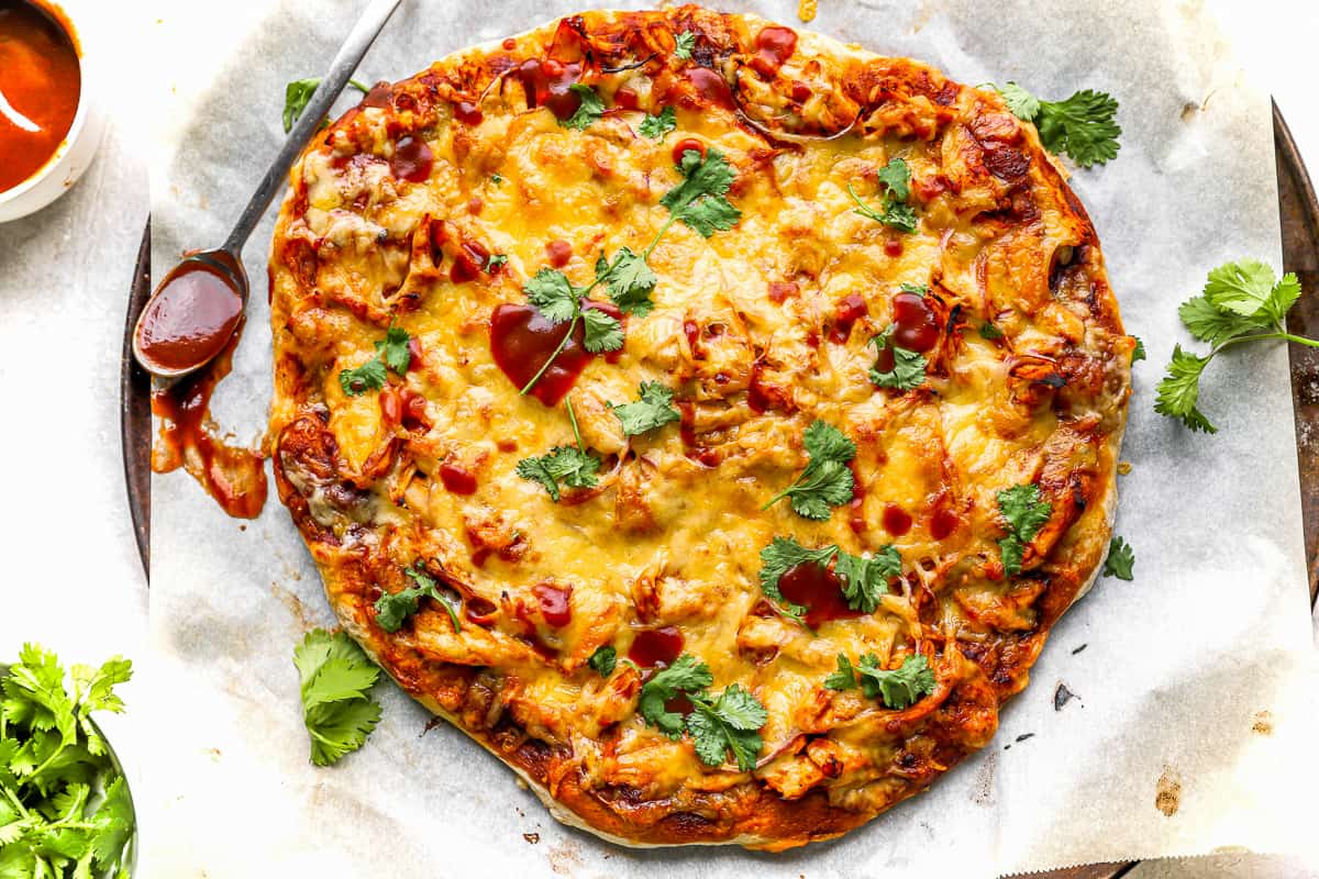 a whole barbecue chicken pizza on a pan lined with parchment paper.