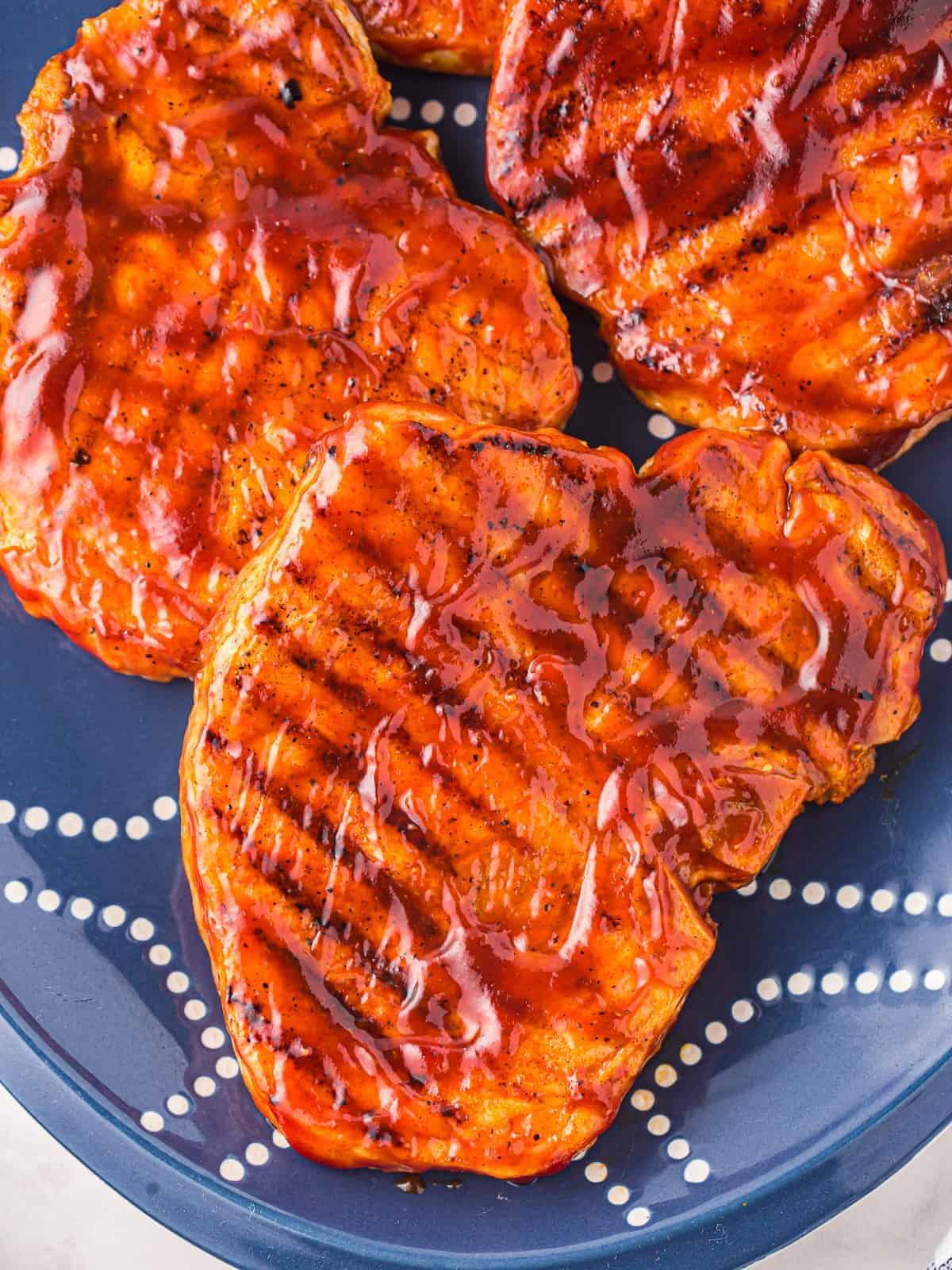 three-quarters view of grilled pork chops covered in bbq sauce on a blue plate.