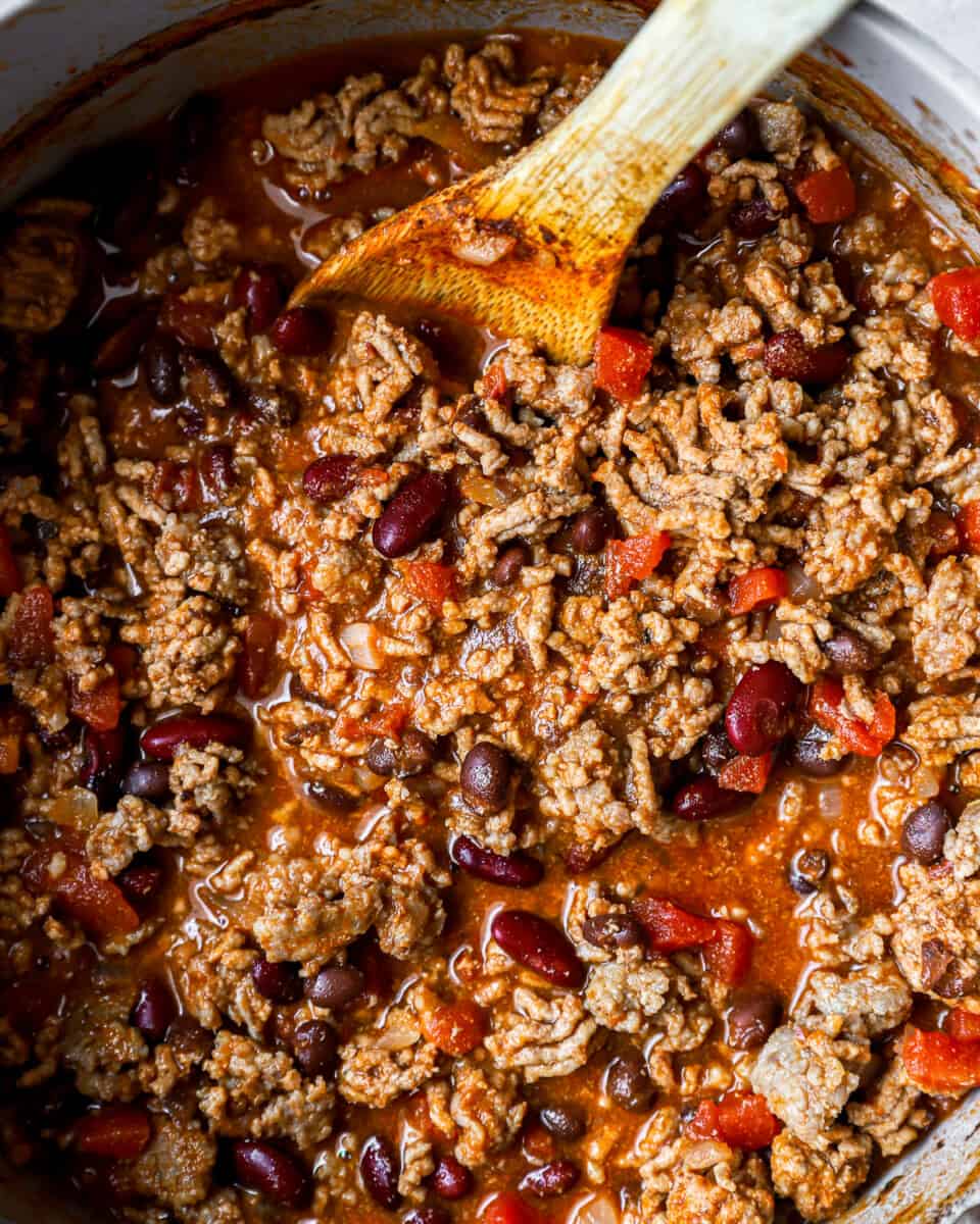 chili in a slow cooker with a wooden spoon.