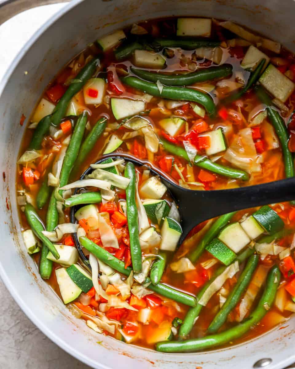 partial overhead view of cabbage soup in a dutch oven with a serving spoon.