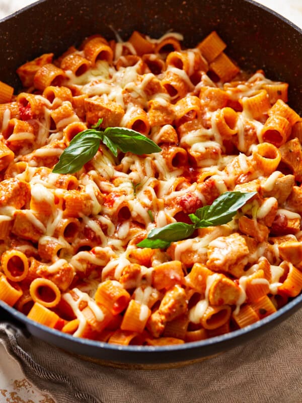 a skillet full of pasta with chicken and basil.