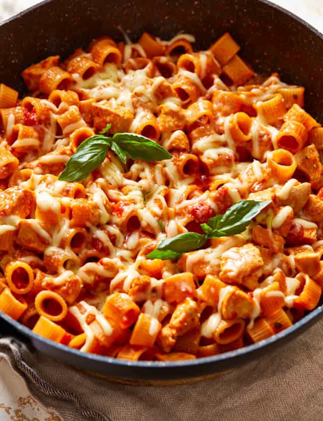 a skillet full of pasta with chicken and basil.