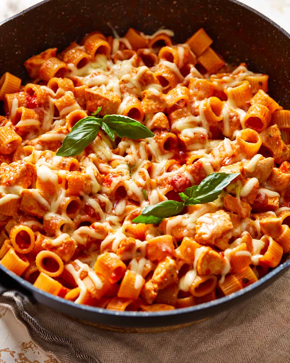 a skillet full of pasta with chicken and basil.