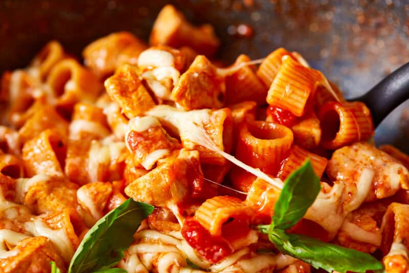 a pan full of pasta with chicken and basil.