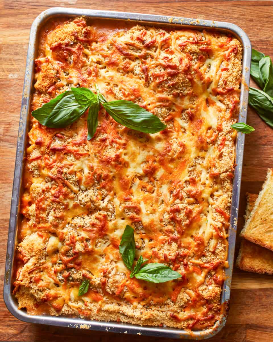 a lasagna with cheese and basil on a wooden table.