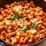 a skillet full of pasta with chicken and basil.